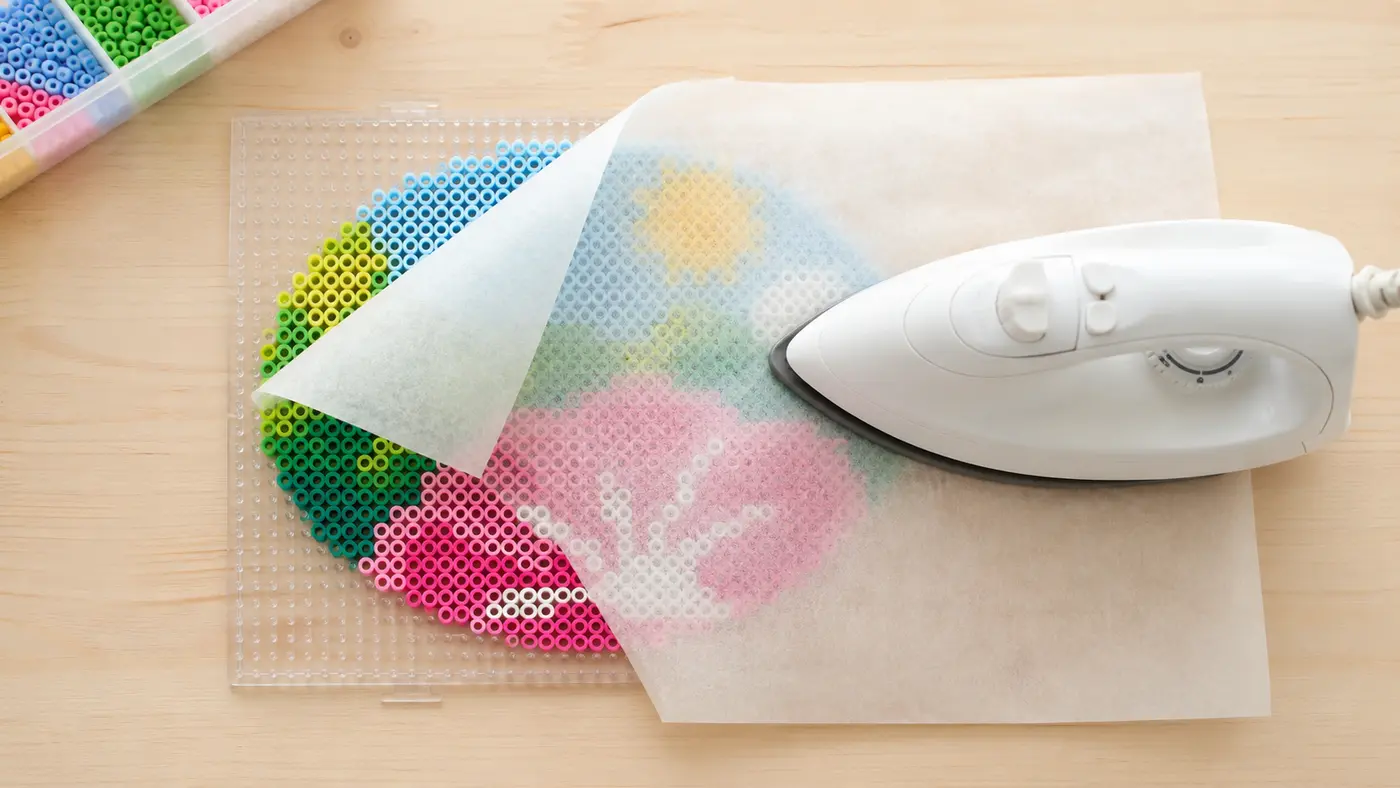 Craft iron fusing a colorful Perler bead pegboard through ironing paper on a light wood table